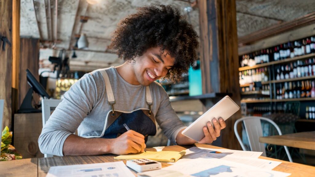 Small business owner reviewing paperwork and asking whether to hire a bookkeeper or keep doing it themselves