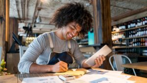 Small business owner reviewing paperwork and asking whether to hire a bookkeeper or keep doing it themselves