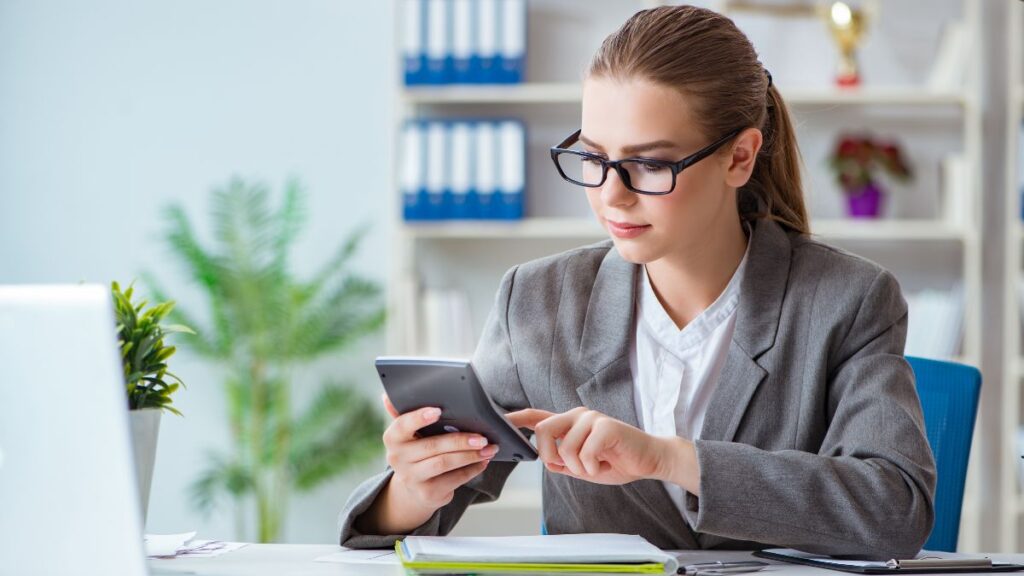 Small business owner reviewing paperwork and asking whether to hire a bookkeeper or keep doing it themselves